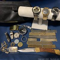Full lot overview showing all watches, bands, pocket knife, whistles, watch parts, and accessories arranged on blue surface with black leather bag