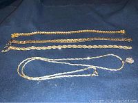 Four pieces of sterling silver jewelry including three bracelets and one necklace laid on dark fabric.