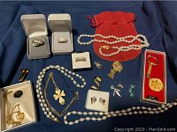 Display of vintage ladies jewelry including pearl necklaces, rings in boxes, enamel cross necklace, earrings, and gold coin keychain.