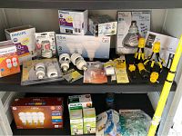 Wide view showing various boxed and loose light bulbs, bulb changers, and small accessories arranged on two shelves.