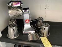 Full view of the manual rotary food cutter and cheese grater with five different cutting drums placed on a black surface.
