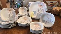 Full view of the stacked plates and bowls including dinner plates, salad plates, small bowls, large bowls, and a platter with floral designs on a wooden table.