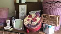 Wide view showing wicker hamper, waste basket, decorative round box, washcloths, and small wicker tray on wooden surface