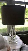 Lamp with crystal base and black shade placed on white side table near window
