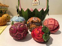 Five small fruit-shaped hand-painted collectible figurines with intricate Jim Shore Heartwood Creek patterns in front of a green basket with floral design