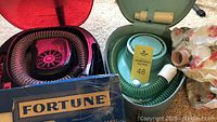 Two vintage hair dryers: blue Lady Sunbeam in teal case and black Select Pro Gold with red lid covering and hoses visible