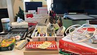 Wide view of office and school supplies on a desk including Webster's dictionary, calculator, glue gun box, crayons, and various stationery items.