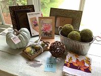 Wide shot of fall decor items including white pumpkin, frames, moss balls, woven ball, votive holder set, and cloth napkin on table near window.