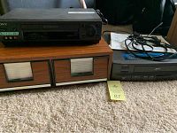 Sony SLV-N500 VCR and Zenith VRM4120 video recorder sitting on top of wooden VHS tape storage unit on carpeted floor