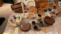 Overall lot view on lace tablecloth containing wooden bowls, pottery mugs, glass dome cheese board and marble paper towel holder