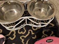 Close-up of two stainless steel dog bowls in a white metal stand on black mat with bone pattern.