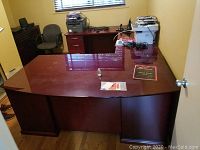 Photo of large wooden office desk in assembled form showing top and drawers. Desk surface shows wear and scratches.
