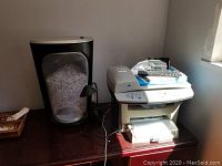 HP LaserJet 3055 all-in-one printer scanner fax on a dark brown desk with Fellowes paper shredder to the left, filled with shredded paper, small adjustable desk lamp, Palm wireless keyboard and a hole puncher on top of printer.