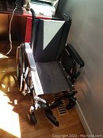 Left front side view of the wheelchair showing seat, armrest, two front wheels and one rear wheel.