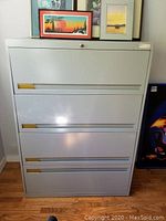 Front and angled view of the 4-drawer metal filing cabinet. Shows locking keyhole and brass-colored handle accents.