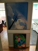 Overall view of larger painting showing tree branches and sky clouds, smaller floral painting visible below