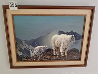 Full view of framed painting showing two mountain goats against rocky mountainous background with some marks on frame and painting surface.