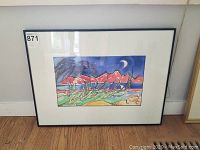 Framed artwork featuring stylized landscape, birds, and mountains under crescent moon. Photo shows full view of framed piece on floor against wall.
