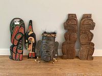 Overview of five carved wooden Indigenous artworks: two painted panels, one mask, two unpainted panels