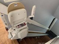 Beige seat and white armrests mounted on silver rail installed on wooden staircase