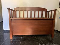 Front view of wooden storage bench with slatted backrest and armrests.
