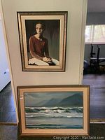 Portrait painting of a seated woman in a frame on the wall above a seascape painting on the floor.