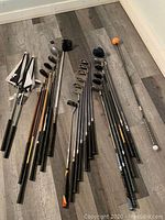 Wide shot of all golf clubs, headcovers and swing trainer on floor