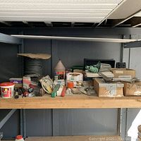 Wide shot of assorted hardware items and tools on a shelf including wire, brushes, adhesives, and small boxes with hardware supplies.