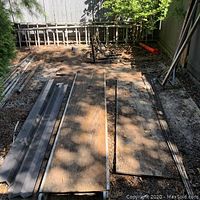 Wide angle showing metal planks and scaffolding boards laid on ground with pipes scattered.