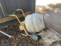 Side view of cement mixer showing yellow steel frame, motor housing, two wheels and concrete residue on drum