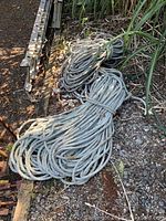 Two large coils of synthetic fiber rope placed on the ground near a metal ladder and plants, showing rope thickness and outdoor condition.