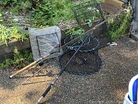 Photo showing two fishing rods, wire mesh fishing traps, and fishing nets placed outdoors on gravel.