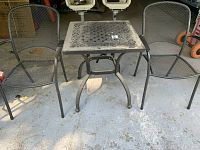 Full view of metal patio table with two metal mesh chairs surrounding it on concrete floor, shows size and condition of the set.