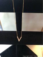 Necklace displayed on a black background to highlight shape and design of V pendant and chain color.