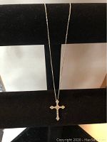 Full view of the silver-tone necklace displayed on a black velvet stand showing the cross pendant with clear crystals.
