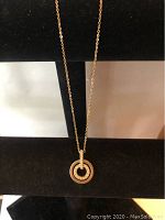 Front view of the gold-tone necklace with circular pendant featuring Swarovski crystals, displayed on black stand.