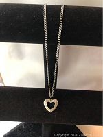 Full view of the silver chain with the open heart pendant studded with clear crystals against a black background.