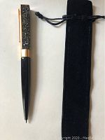 Swarovski pen showing the crystal-embellished rose gold clip and black body alongside black velvet pouch case.