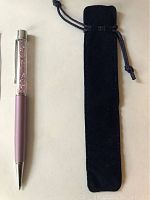 Top view of purple pen next to black velvet drawstring case on white background.