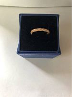 Rose gold-colored Swarovski crystal ring shown in blue jewelry box with black velvet interior.