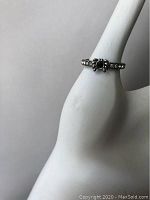 Silver ring with spider design featuring black and clear crystals shown on white hand-shaped display stand.