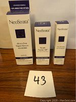 Photo of three boxed NeoStrata skincare products including All-in-One Night Serum, Youth Factor GF, and Anti-Wrinkle Lip Enhancer arranged upright on wooden surface with lot number card.