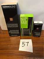 Three boxed skincare items on wooden surface with lot number 57: Dermablend Professional Leg and Body Makeup, Nip+Fab Smooth One Step Primer, and Dermablend Quick Fix Concealer.