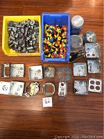 Top down view of metal electrical boxes, assorted wire connectors in various colors, and switch plates laid out on a wooden surface.