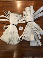 Two bunches of folded white fire hose secured with black ties on wooden floor.