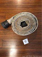 Coiled white fire hose laid on wooden floor with black connectors visible, showing the full length and condition of the hose.