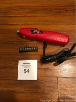 Red Skil cordless power screwdriver on wooden floor with charging cord and 10-piece bit set in black holder annotated with MaxSold auction lot number.