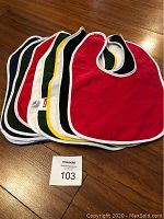 Lot of 10 assorted colored baby bibs made of 100% cotton with white trim and snap closure, laid out on wooden surface.
