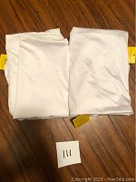 Four white pillow case slips folded, showing yellow brand tags, laid on wooden floor.