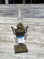 Full view of the antique brass oil lamp with glass chimney on a weathered wooden surface.